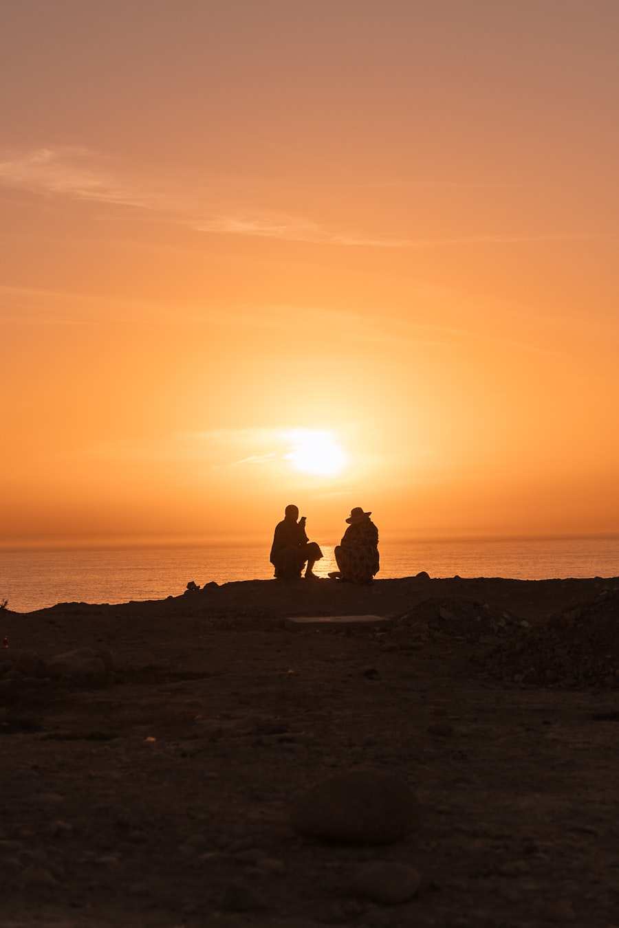 Two people sitting on a headland, watching the sun drop into the sea