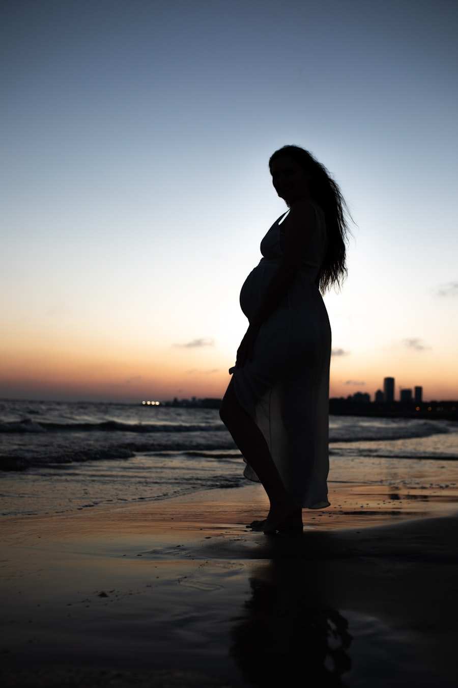 A pregnant woman standing at the edge of the water as the light goes