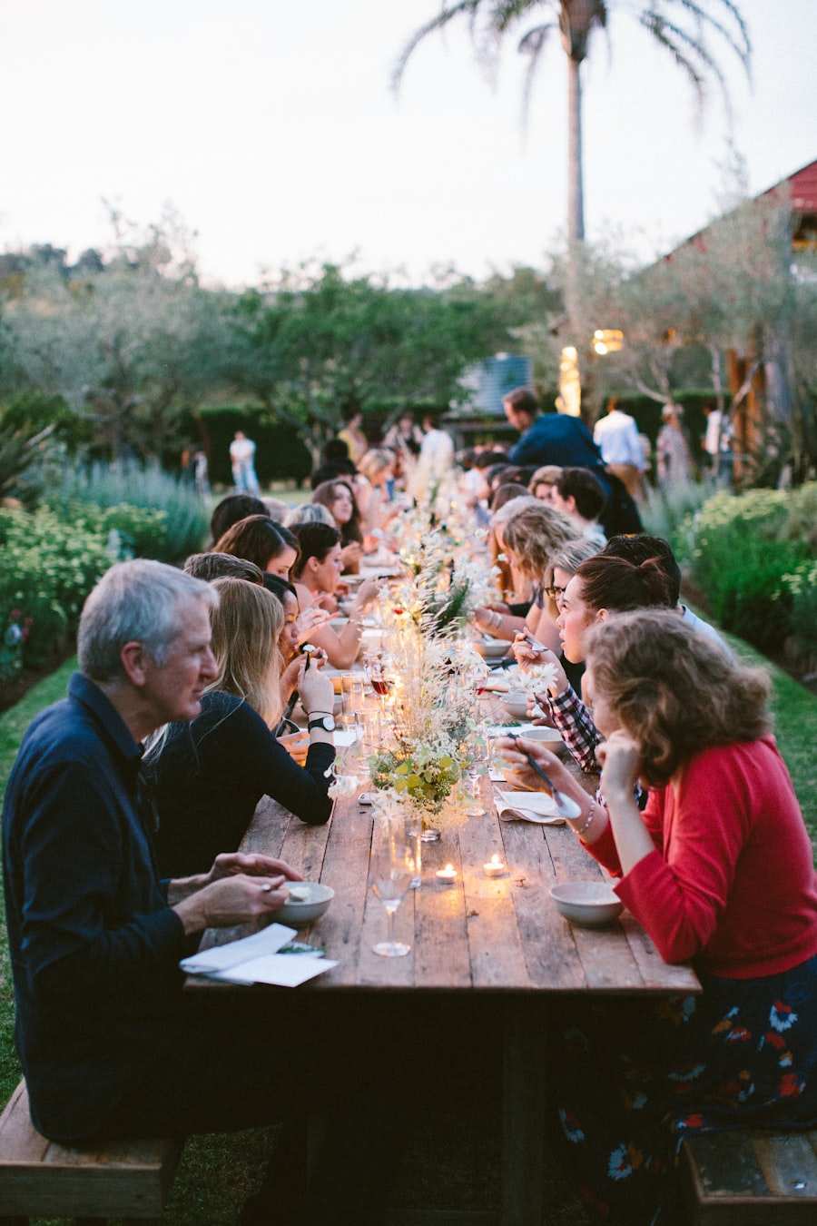 A long table of people eating together outdoors as the light goes
